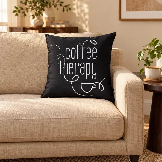 Față de pernă decorativă neagră cu mesajul „Coffee Therapy” pe canapea